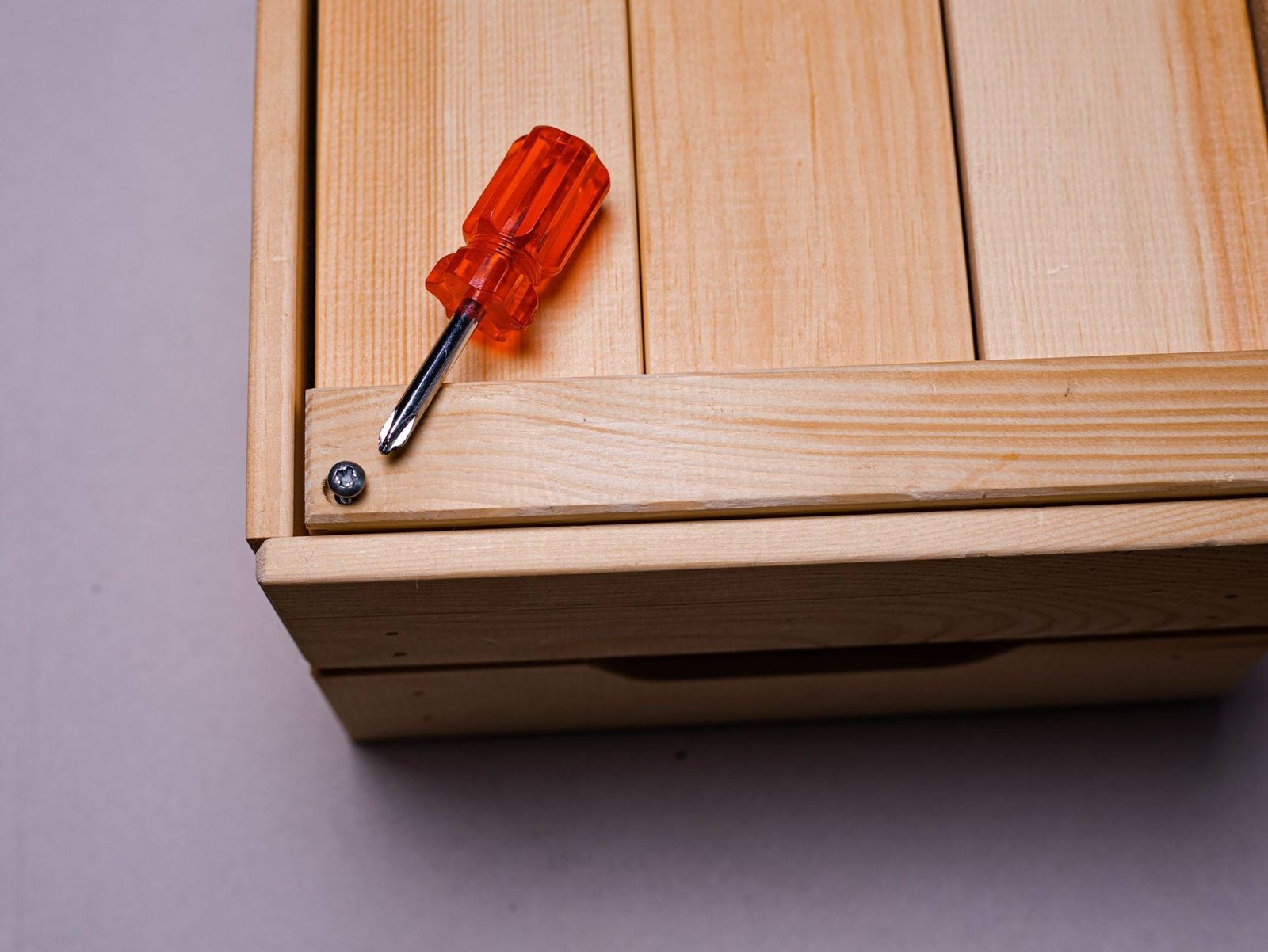 Minimalist image of an orange screwdriver beside a screw on a wooden box