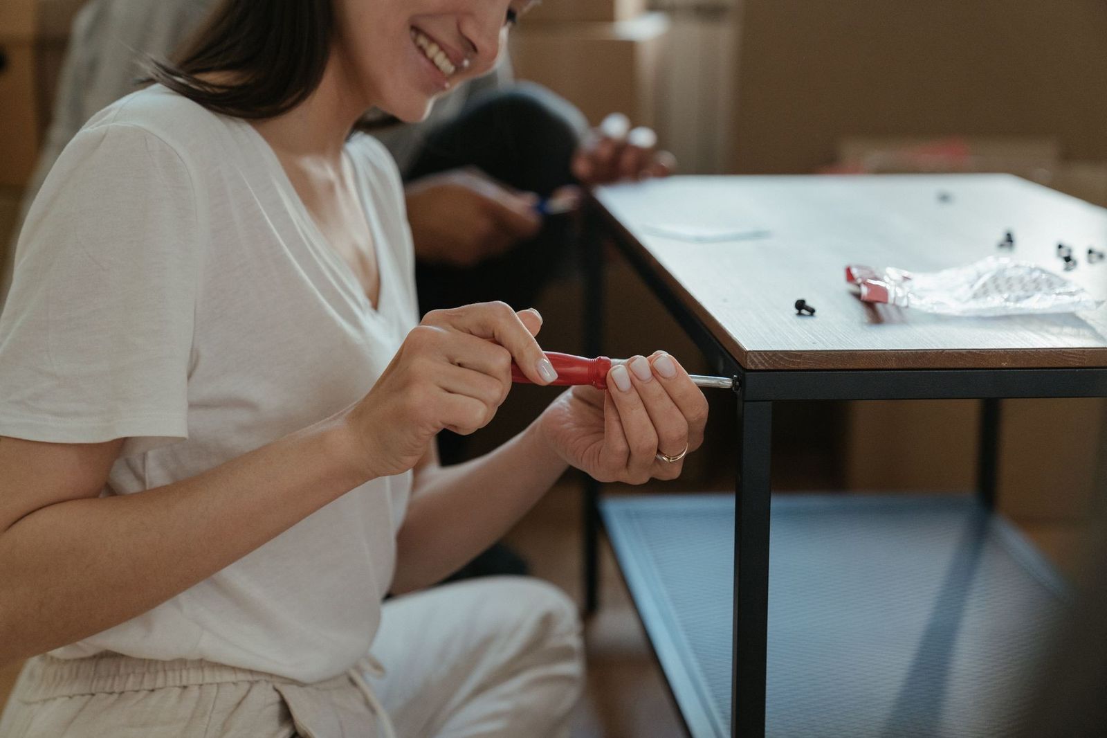 Woman smiling while assembling a table using a screwdriver in a home setting.